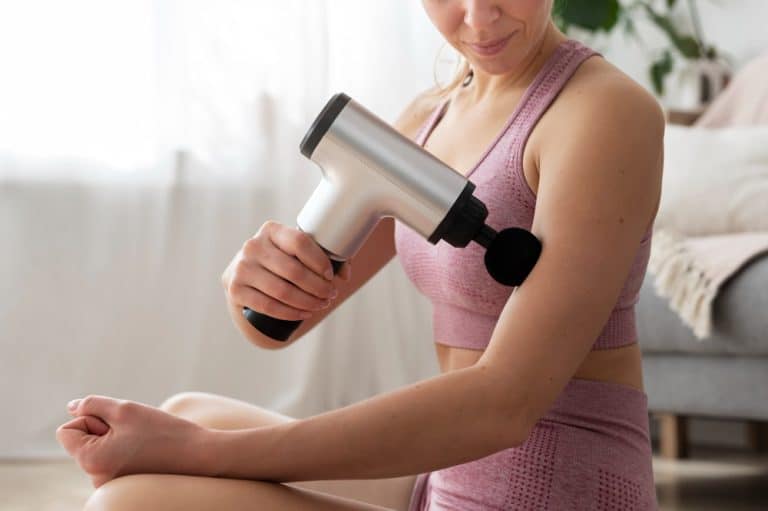 mujer pasandose pistola de masaje en biceps