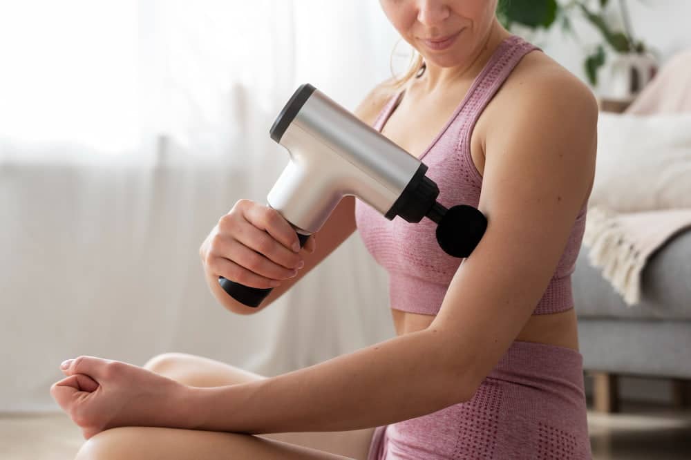 mujer pasandose pistola de masaje en biceps