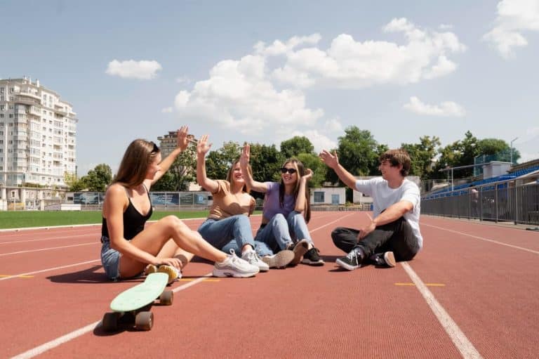 Estudiantes en pista atletismo sentados chocando los cinco