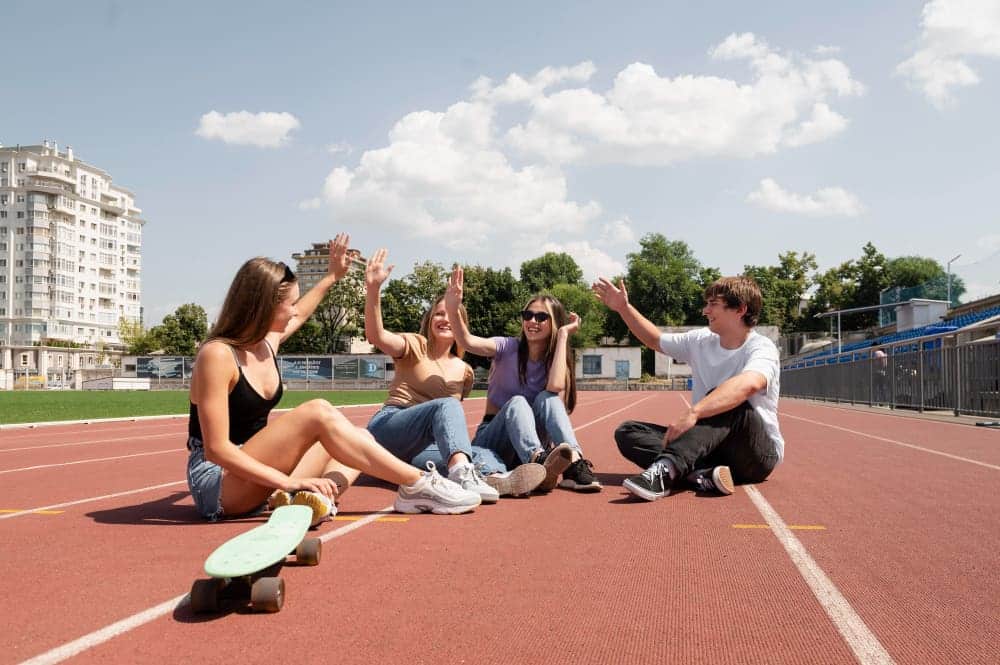 Estudiantes en pista atletismo sentados chocando los cinco